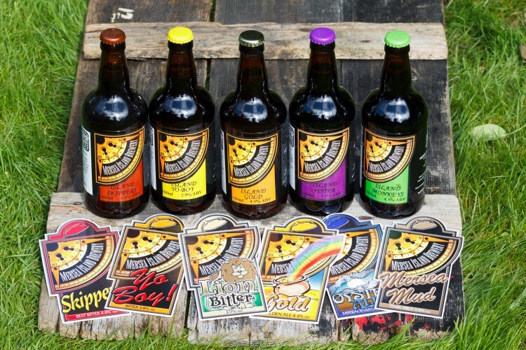 Colourful Bottles of Mersea Island Beer sit on a branded box on the grass